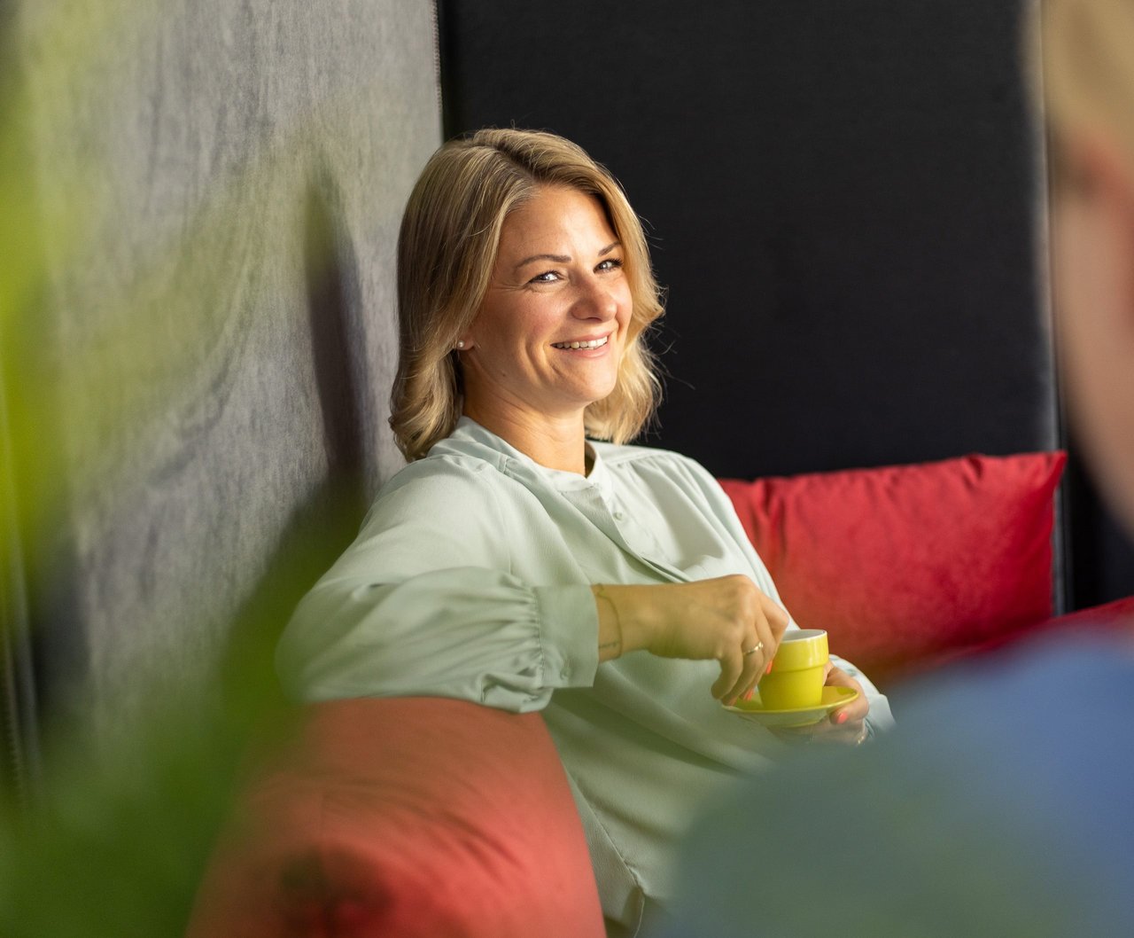 Zwei Mitarbeiterinnen der Insolvenzkanzlei sitzen an einem Besprechungstisch und lächeln in die Kamera