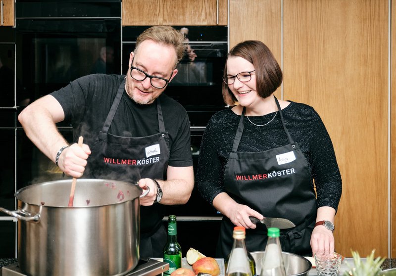 Impressionen vom gemeinsamen Kochen bei der Weihnachtsfeier der Kanzlei – Ein Mitarbeiter rührt im Kochtopf und eine Kollegin kocht